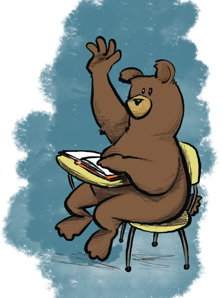 A brown bear sits at a yellow school desk with an open book, hand raised high to answer.